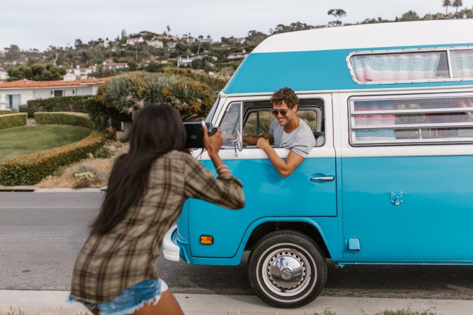 a woman taking her partner's photo on a blue VW Bus
